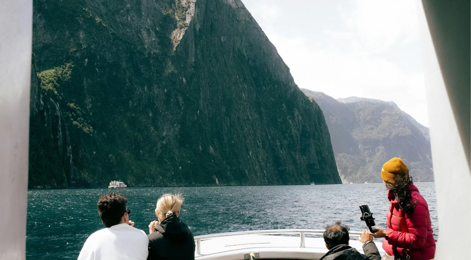 Tourists on a boat deck photographing Milford Sound's towering cliffs
